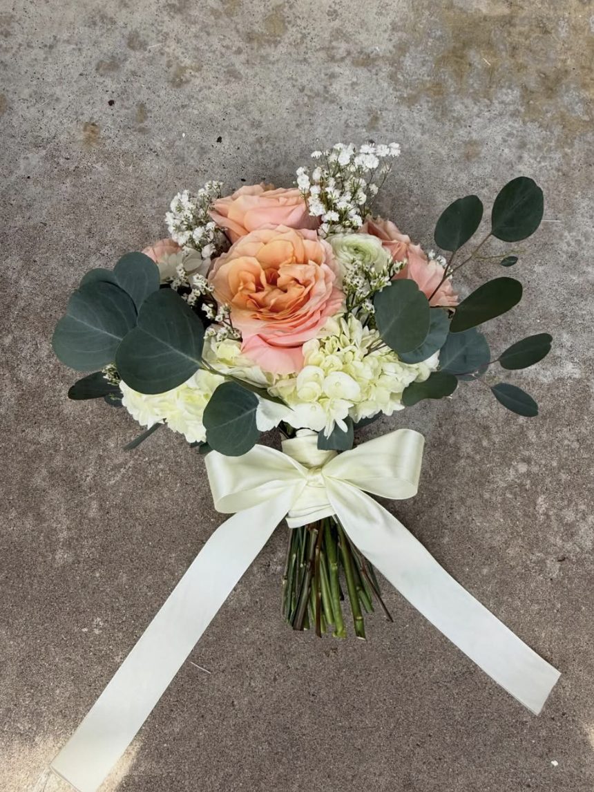 A signature blush and peach wrapped bouquet with eucalyptus and an ivory ribbon, by Flowers by Syd